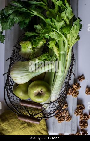 Von oben Metallkorb mit Äpfeln, Sellerie, Fenchelknollen und Walnüssen an Bord vor weißem Hintergrund angeordnet Stockfoto