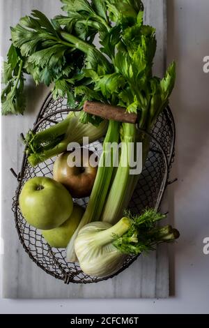 Von oben Metallkorb mit Äpfeln, Sellerie, Fenchelknollen und Walnüssen an Bord vor weißem Hintergrund angeordnet Stockfoto