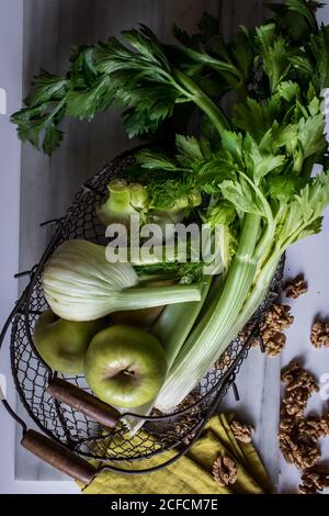 Von oben Metallkorb mit Äpfeln, Sellerie, Fenchelknollen und Walnüssen an Bord vor weißem Hintergrund angeordnet Stockfoto