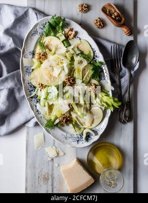 Von oben Gericht mit köstlichen Salat aus Äpfeln, Parmesan-Käse, Walnüssen, Sellerie und Öl auf weißem Hintergrund Stockfoto