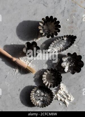 Draufsicht auf verschiedene Metall-Backformen und kleine Küche Pinsel auf Marmortisch mit weißem Mehl bestreut Stockfoto