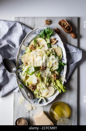 Von oben Gericht mit köstlichen Salat aus Äpfeln, Parmesan-Käse, Walnüssen, Sellerie und Öl auf weißem Hintergrund Stockfoto