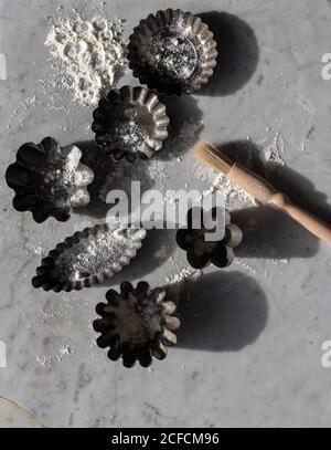 Draufsicht auf verschiedene Metall-Backformen und kleine Küche Pinsel auf Marmortisch mit weißem Mehl bestreut Stockfoto