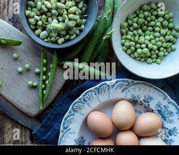 Oben vom Seil frische grüne Erbsen in der Schüssel und Eier auf Holztisch beim Kochen Stockfoto