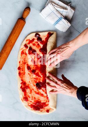 Von oben beschnitten unkenntlich Person Hände, die frische Erdbeer Brioche Auf einer Küche weißen modernen Marmortisch Stockfoto