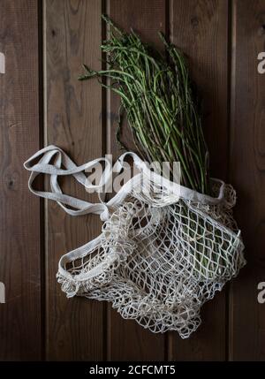 Von oben weißer Saitenbeutel mit großem Bündel Frischer grüner Spargel auf Holztisch Stockfoto