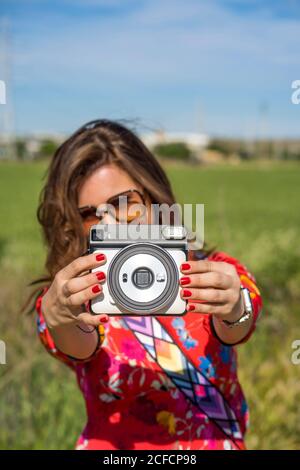 Junge Frau demonstriert Instant-Kamera, während in Wiese auf Sonniger Sommertag Stockfoto