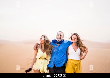 Älterer bärtiger Mann lachte und umarmte fröhliche Frauen beim Gehen In sandiger Wüste während der Reise in Marokko Stockfoto
