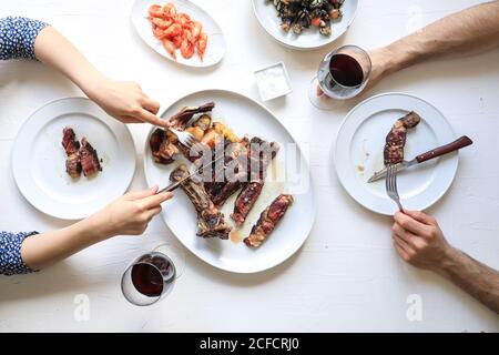 Von oben Ernte Menschen schneiden Fleischsteak und genießen rot Wein beim Essen schmackhafte Mahlzeit Stockfoto