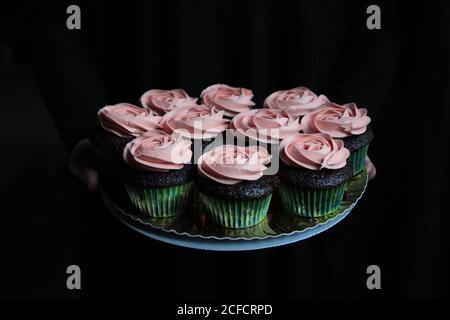 Leckere süße Cupcakes mit rosa Creme auf dem Teller angeordnet dekoriert Auf schwarzem Hintergrund Stockfoto