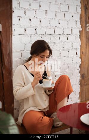 Friedliche Frau, die Kaffee trinkt, während sie sich zu Hause ausruhte Stockfoto