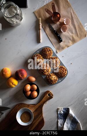 Von oben Zusammensetzung von leckeren Cupcakes mit Walnüssen im Backen Teller Eier Pfirsiche Mehl und Pergamentpapier auf weiß angeordnet Oberfläche Stockfoto