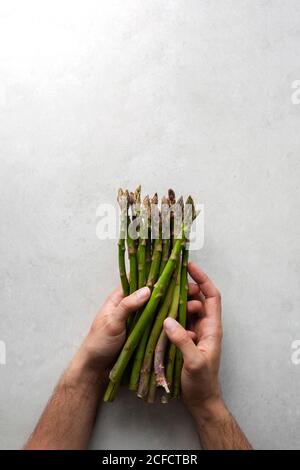 Blick von oben auf Ernte anonymen Koch hält Bündel von frischen Grüner Spargel beim Zubereiten von Speisen am grauen Marmortisch Küche Stockfoto
