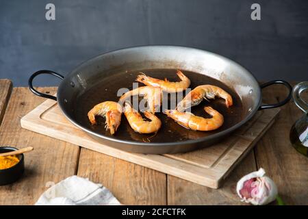 Von oben appetitlich geröstete Garnelen in Öl auf Großmetall Pfanne auf Schneidebrett auf rustikalem Holztisch in der Küche Stockfoto