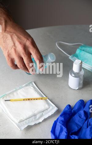Von oben männlicher Therapeut im medizinischen Gewand sitzend am Tisch Im Krankenhaus und desinfizieren Hände mit antiseptischen während der Vorbereitung Behandlung von Patienten während des Coronavirus-Ausbruchs Stockfoto