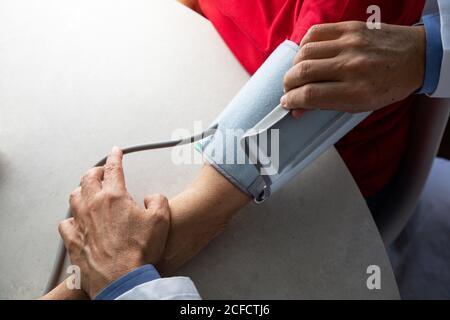 Von oben des Getreidearztes mit Stethoskop, das am Tisch sitzt Im medizinischen Raum und Messung des Blutdrucks mit Tonometer während Arbeiten im Krankenhaus während des Coronavirus-Ausbruchs Stockfoto
