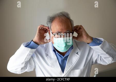 Ältere Arzt in weißem medizinischen Kleid trägt Gesichtsmaske, während Arbeiten im Krankenhaus während des Coronavirus-Ausbruchs Stockfoto