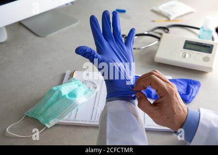 Von oben der Ernte männlichen Hausarzt setzen auf Einweg Chirurgische Handschuhe während der Arbeit in der Klinik während covid 19 Pandemie Stockfoto