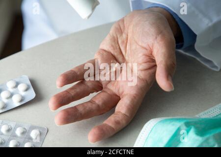 Draufsicht des männlichen Therapeuten im medizinischen Kleid sitzend an Tisch im Krankenhaus und desinfizieren Hände mit antiseptischen während der Vorbereitung Zur Behandlung von Patienten während des Coronavirus-Ausbruchs Stockfoto