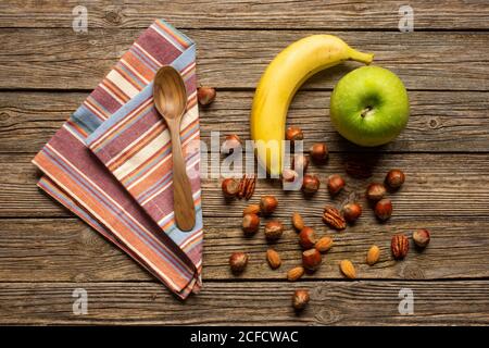 Draufsicht auf Apfel und Banane mit Nüssen in der Nähe von Löffel Und Handtuch auf Holztisch mit gesunden Lebensmitteln Stockfoto
