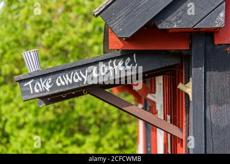 Kaffeetasse steht auf Baldachin mit Take Away Kaffee Schriftzug, Holzhaus im Tor Stockfoto