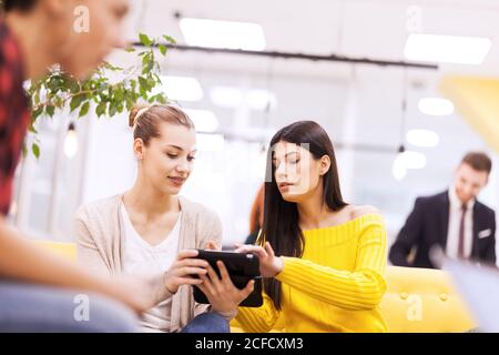 Zwei schöne junge Geschäftskolleginnen, die in einem modernen Büro chatten. Erfolgreiches Startup-Team mit einem Brainstorming-Meeting Stockfoto