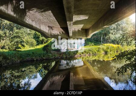 Architektur, Technik und Natur, unter einer Brücke, Brückenkopf, Überbau mit Spiegelung im Wasser, Betonbrücke über die Ilmenau, Stockfoto