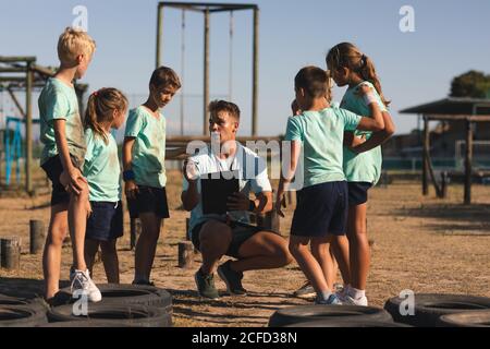 Männlicher Fitness-Trainer, der Kinder in einem Boot Camp unterweist Stockfoto