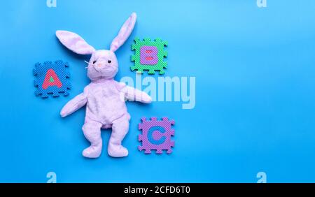 Kaninchen Spielzeug mit englischen Alphabet Puzzle auf blauem Hintergrund. Bildungskonzept, Kopierbereich Stockfoto