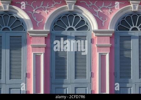 Die Vorderseite eines pinkfarbenen, sino-portugiesischen oder Peranakan-artigen Hauses mit grauen Gitterfenstern, in der Thalang Road in der Altstadt von Phuket Town, Thailand Stockfoto