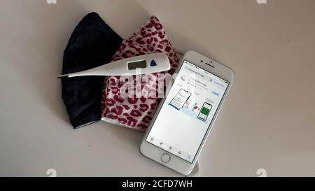 Corona Warnung App auf dem iphone und Mund-Nase Maske auf dem Tisch Mit klinischem Thermometer Stockfoto