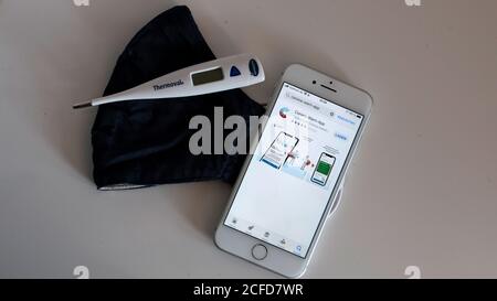 Corona Warnung App auf dem iphone und Mund-Nase Maske auf dem Tisch Mit klinischem Thermometer Stockfoto