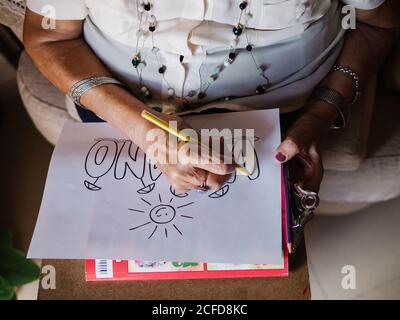 Von oben von älteren grauhaarigen Weibchen in weißem Hemd Und Gläser zeichnen auf Papier mit Bleistift sitzen auf Sessel Zu Hause Stockfoto