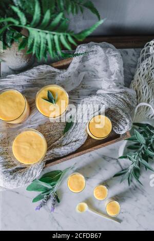 Leckere aromatische Mango-Mousse in Glaskrügen und Löffel auf Tisch mit grünen Pflanzen dekoriert Stockfoto