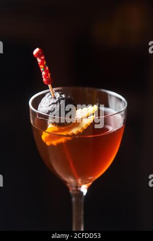 Roter Alkoholcocktail Manhattan garniert mit Kirsche und Orangenschale Auf Stick vor dunklem Hintergrund Stockfoto