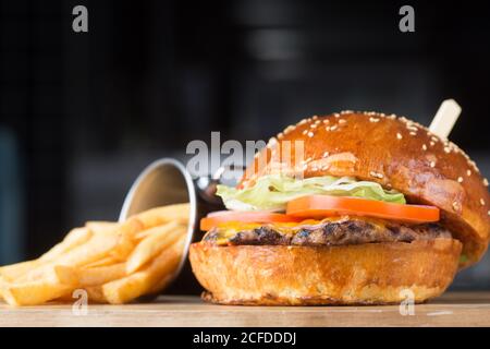 Teller mit gehacktem Rotkohl und Schüssel mit Sauce platziert In der Nähe leckere Burger mit Salat und Tomaten auf Patty und Eimer Pommes im Café Stockfoto