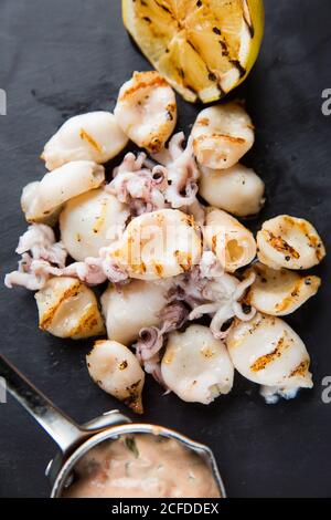 Haufen von leckeren gegrillten Tintenfische und kleine Oktopusse in der Nähe platziert Zitrone und Sauce auf dem Tisch im Café Stockfoto