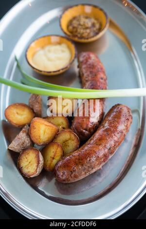 Von oben Stücke von leckeren gegrillten Kartoffeln und saftigen Würsten Mit frischem Frühlingszwiebel auf Metallplatte in der Nähe von Schüsseln mit platziert Saucen in der Cafeteria Stockfoto