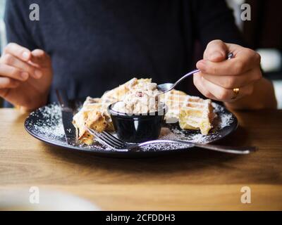 Unkenntliche Person, die kaltes, süßes Eis und frische Waffeln genießt Während des Mittagessens im Café Stockfoto