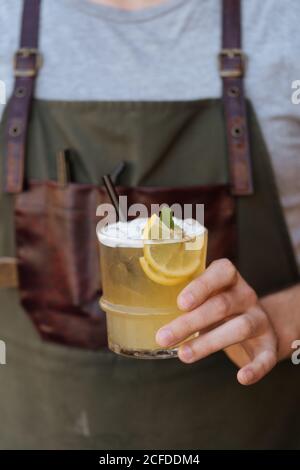 Crop Barista in Schürze hält Glas von frischen saftigen Limonade Dekoriert mit geschnittenen Zitronen und grüner Minze Stockfoto