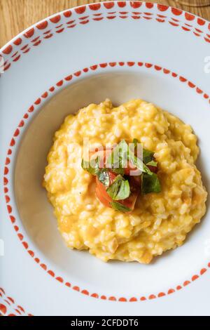 Von oben appetitlich Risotto mit Kürbis mit geschnittenen Tomaten verziert Und grün in Zierteller auf Tisch Stockfoto