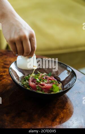 Crop Cook Gießen appetitliche Sauce in Salat von Lachs und grüne in Glasplatte auf Tisch Stockfoto