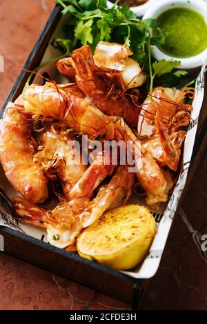 Von oben gebackene große Garnelen in quadratischer Platte mit Zitrone frische Petersilie und grüne Sauce im Restaurant Stockfoto