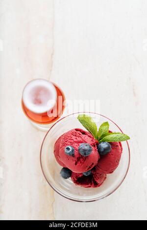 Von oben aus lila Kugeln Eis im Glas Schüssel mit frischer Blaubeere und Minze dekoriert und serviert mit Ein Glas rotes Getränk im Restaurant Stockfoto