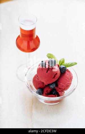 Von oben aus lila Kugeln Eis im Glas Schüssel mit frischer Blaubeere und Minze dekoriert und serviert mit Ein Glas rotes Getränk im Restaurant Stockfoto