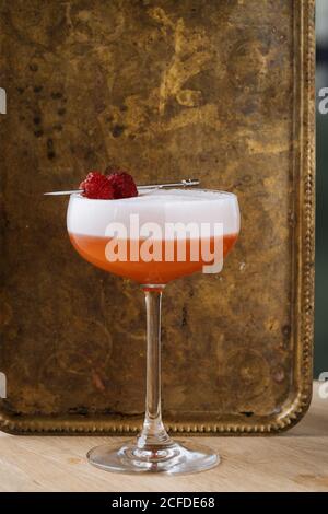 Farbenfroher roter Alkoholcocktail in stilvollem Glas auf Tisch mit Bar Löffel und Sieb im Restaurant Stockfoto