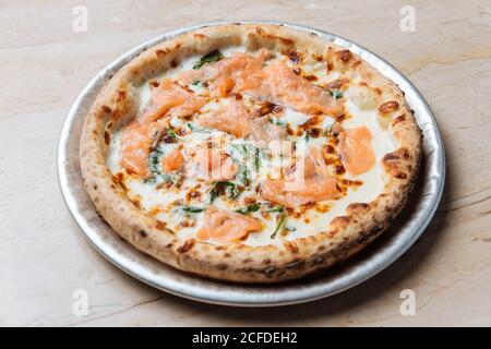 Blick von oben auf frisch gebackene Pizza mit Käse und Scheiben Von rotem Fisch mit Kräutern im Restaurant dekoriert Stockfoto