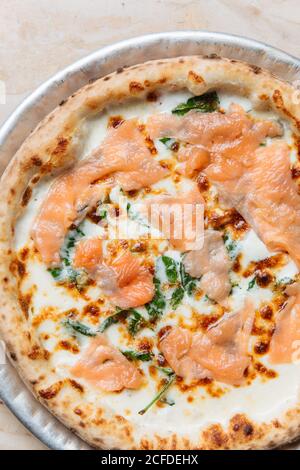 Blick von oben auf frisch gebackene Pizza mit Käse und Scheiben Von rotem Fisch mit Kräutern im Restaurant dekoriert Stockfoto