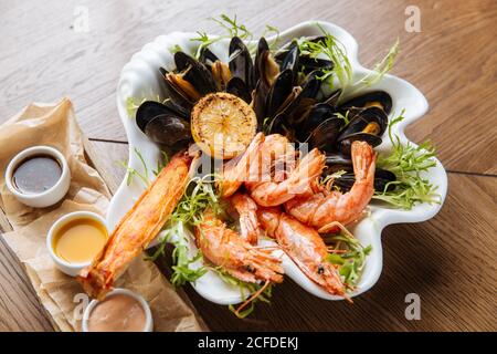 Von oben köstliche gegrillte Garnelen und Muscheln mit Gemüse Serviert auf weißem Teller mit drei Saucen auf der Seite Stockfoto