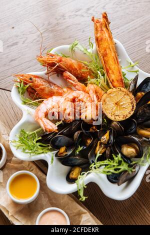 Von oben köstliche gegrillte Garnelen und Muscheln mit Gemüse Serviert auf weißem Teller mit drei Saucen auf der Seite Stockfoto